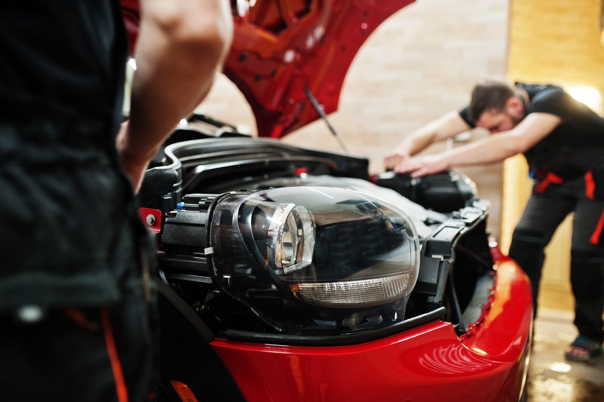 Neil Arnold Tyres And Autos Mechanic inspecting damaged headlight of red car