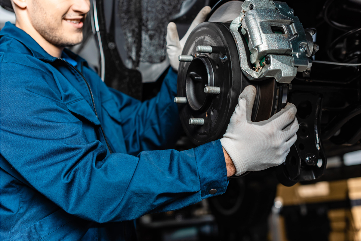 Neil Arnold Tyres And Autos Mechanic inspecting car brake rotor and caliper during auto repair.