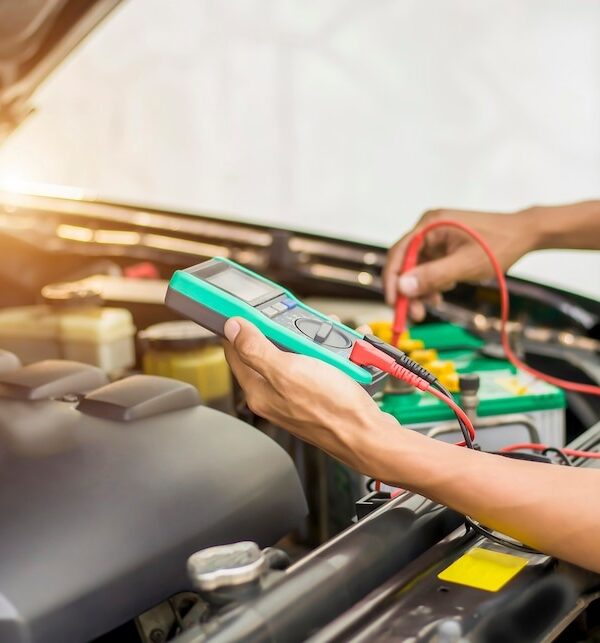 Neil Arnold Tyres And Autos Mechanic checking car battery voltage with a multimeter.