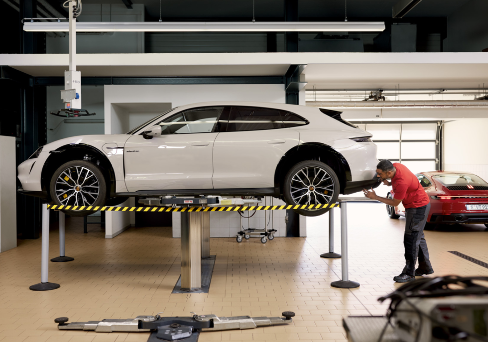 White Porsche Taycan Cross Turismo on a car lift in a service garage with Neil Arnold Tyres Mechanic